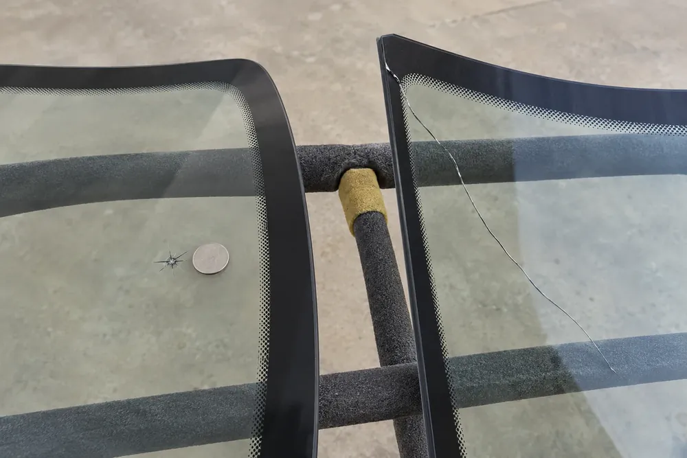 Small star-shaped windshield chip beside a coin and a long crack reaching another pane's edge.