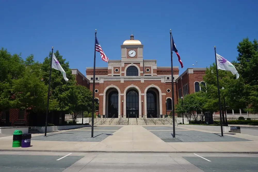Lewisville City Hall with a clock tower and flags behind a paved plaza in Lewisville, Texas